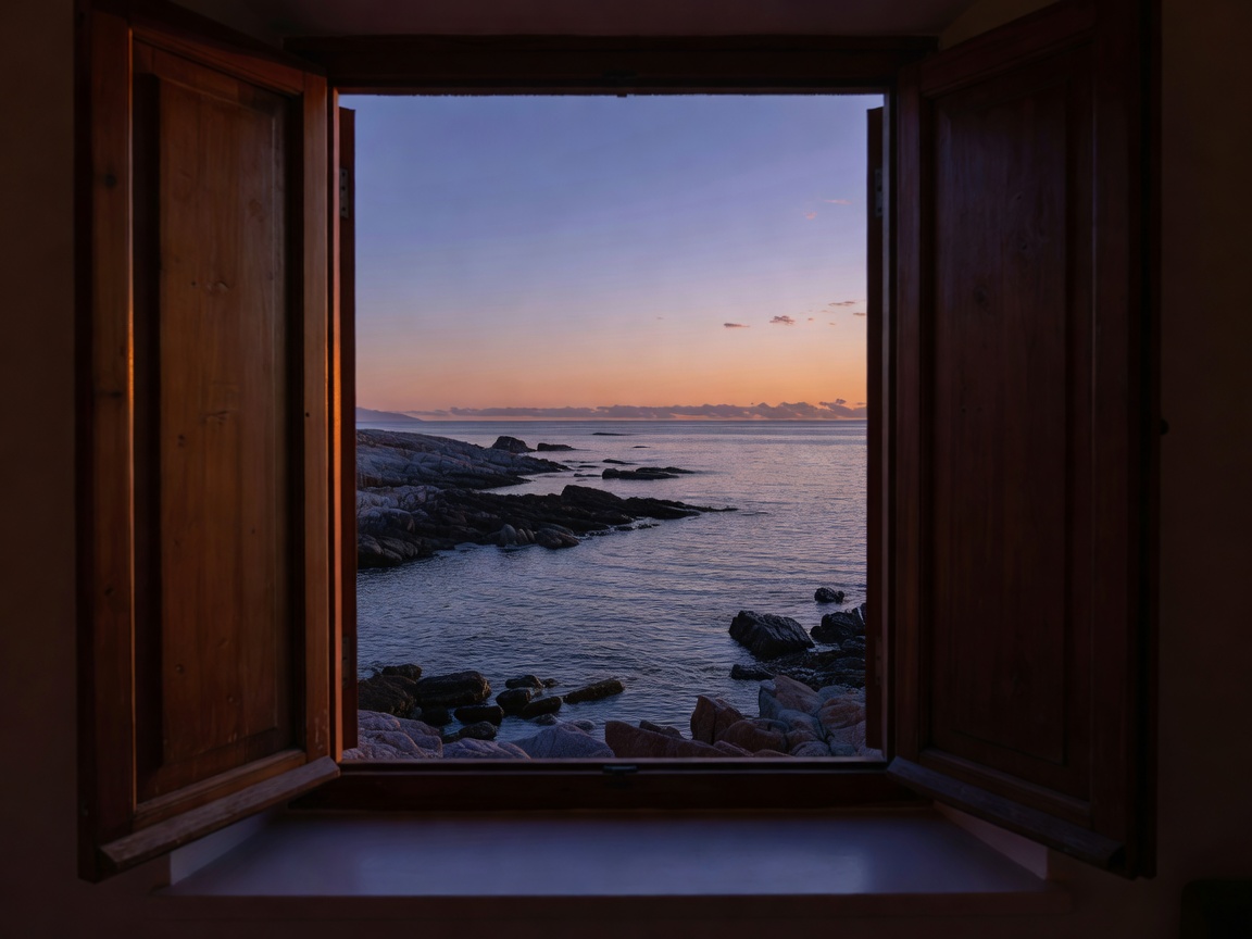 View of a rocky bay through the open shutters of a hotel window at dusk